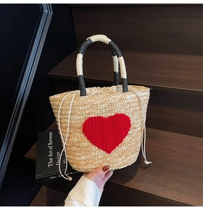 Detail of woven straw bag featuring a red heart motif and black and white striped handle