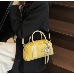 Detail of yellow pebbled leather Boston bag with pearl bow charm on a model