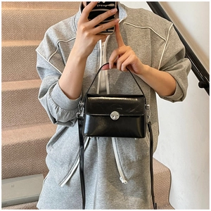 Close-up of black glossy oil wax leather bag featuring a round silver metal twist lock