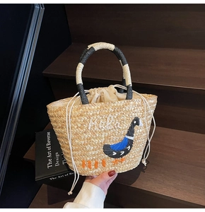 Detail of woven straw handbag featuring peacock embroidery and a cream drawstring closure