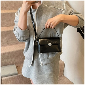 Detailed close-up of glossy black crossbody bag with round silver metal twist lock
