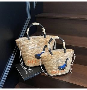 Detail of straw beach bags with bird embroidery and black-white woven handles