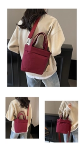 Deep red canvas tote bag with top handles and adjustable strap worn by model in detail