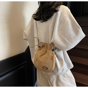 Detail of khaki drawstring bucket bag with black LUCKY patch and orange side tag accent