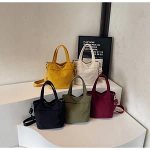 Multiple colors of canvas tote bags with adjustable straps displayed on a white stand