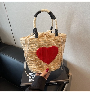 Macro shot of a handmade straw bag featuring a red heart motif and black-white handles