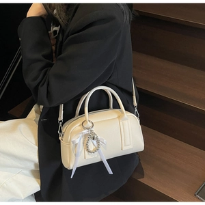 Close-up of cream Boston bag with lychee texture, silver heart charm, and ribbon detail