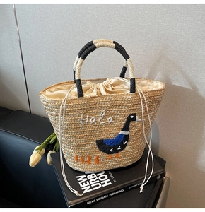 Detailed close-up of handmade straw tote with goose embroidery and Hola text detail