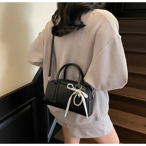 Chic black Boston bag detail featuring pearl charm and white ribbon on textured leather