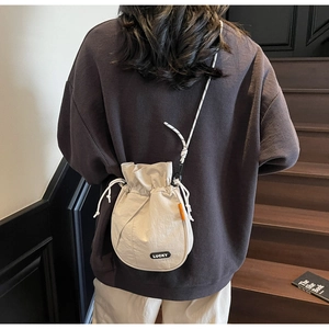 Detail view of cream drawstring bucket bag with black LUCKY patch and orange woven tag