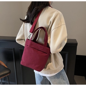 Detail view of burgundy canvas crossbody bag with adjustable wide shoulder strap and handle