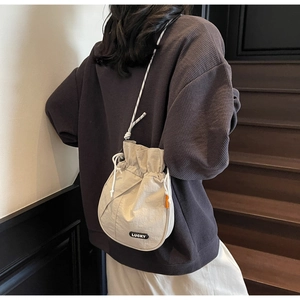 Detail of off-white drawstring bucket bag with black LUCKY tag and bicolor cord strap