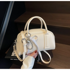 Detail of a creamy white Boston bag with litchi grain texture and heart charm decoration