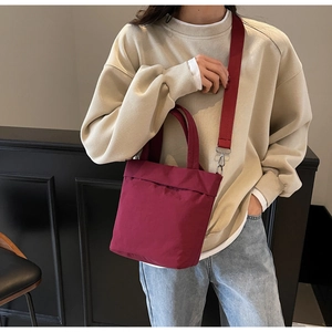 Close-up of a burgundy nylon crossbody bag worn by a model in a minimalist urban style