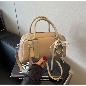 Close-up of khaki Boston bag with pebble leather texture, silver hardware and ribbon charm