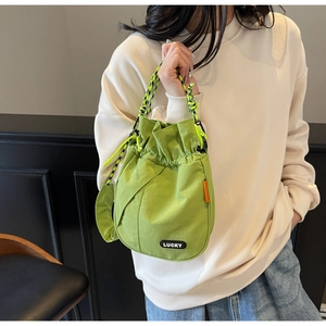 Detail of green drawstring bucket bag with colorful woven handle and LUCKY logo patch