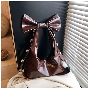 Detail einer braunen Lackleder-Schultertasche mit Nieten und einem großen Schleifengriff