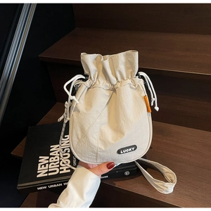 Detail of beige nylon drawstring bucket bag featuring a black LUCKY patch and orange label