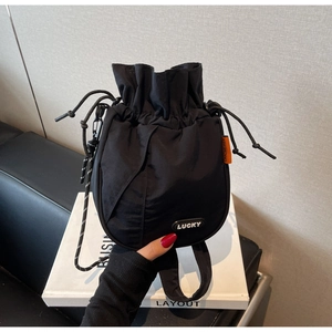 Detail of black drawstring bucket bag featuring a rubberized Lucky patch and orange side tag