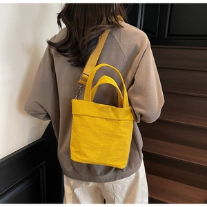 Detail of bright yellow nylon tote bag with adjustable wide strap on a model back