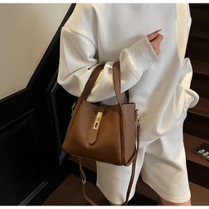 Sac seau chic en cuir marron avec motif litchi porté par un mannequin en décor épuré