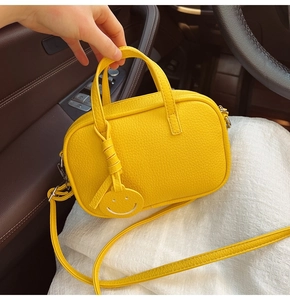 Detail of yellow lychee pattern leather pillow bag with a round smiley face charm
