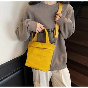 Detail of bright yellow crossbody bag with wide shoulder strap worn by a model