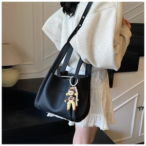 Detail of black lychee grain leather bucket bag with fashion logo and cartoon charm