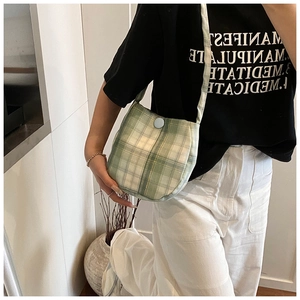 Detail of green plaid fabric crossbody bag featuring a light blue button closure