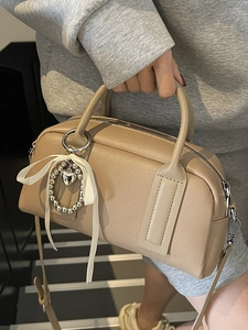 Khaki brown lychee leather Boston bag with bow pendant shown in a lifestyle street setting