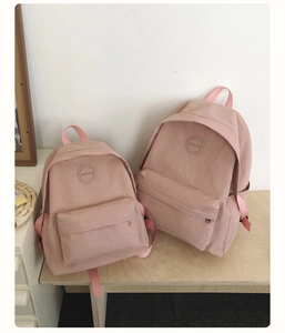 Minimalistische roze nylon rugzak in twee maten op een houten tafelblad gepresenteerd