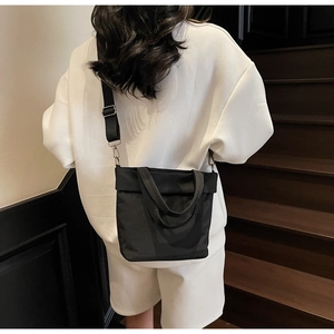 Detail of minimalist black canvas crossbody bag featuring adjustable metal buckle on a shoulder strap