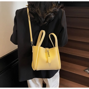 Détail du sac seau jaune à texture litchi avec boucle métallique sur des escaliers en bois