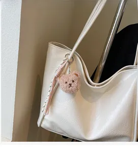Detail of plush bear bag charm with ribbon on white textured oil wax leather tote bag