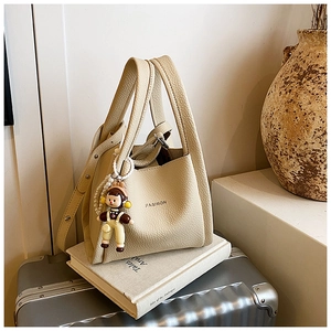 Detail of beige lychee pattern bucket bag with cute doll charm and pearl chain decoration