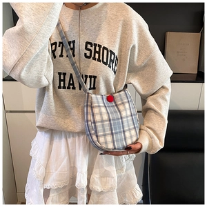 Detail of blue plaid canvas crossbody bag featuring a distinctive red decorative button