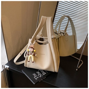 Detail of beige lychee grain bucket bag with FASHION text and cute doll charm
