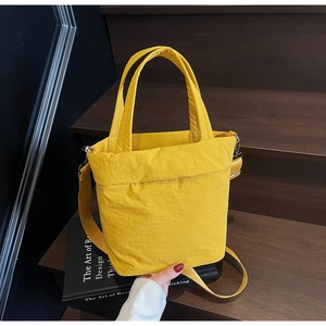 Detail of a yellow nylon tote bag featuring wrinkled texture and adjustable cross-body strap