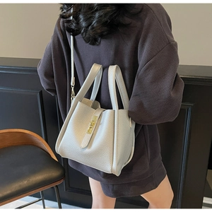 Détail d'un sac seau en cuir gris litchi avec cadenas doré porté par un mannequin