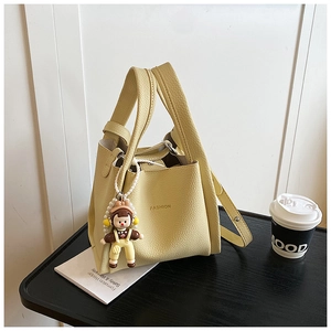 Detail of yellow lychee leather tote bag with FASHION logo and cartoon girl charm