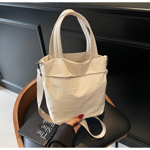 Detailed view of cream nylon tote bag texture with adjustable strap on black background