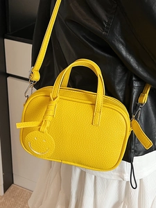 Vibrant yellow faux leather pillow bag with smiley charm and crossbody strap