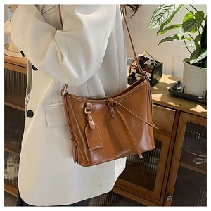 Sac seau marron en cuir huilé avec cordon, porté par un mannequin en blazer ivoire