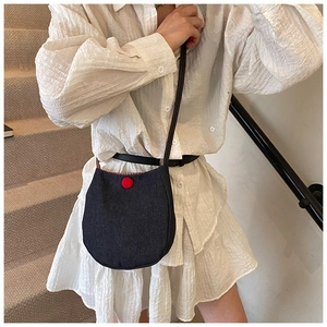 Detail of blue denim crossbody bag featuring a red button closure and checkered lining