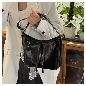 Détail d'un sac seau noir en cuir ciré brillant avec ruban décoratif et bandoulière