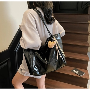 Glossy black oil wax leather tote bag with brown bear charm shown on a staircase