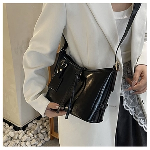 Détail du sac seau noir poli avec quincaillerie dorée et bandoulière sur le modèle