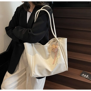 Close-up of white oil wax leather tote bag featuring a cute brown bear plush pendant