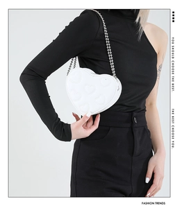 Close-up of white heart-shaped leather crossbody bag with quilted stitching and chain