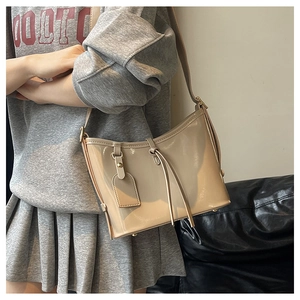Détail du sac seau minimaliste en cuir verni beige avec finition brillante et bandoulière